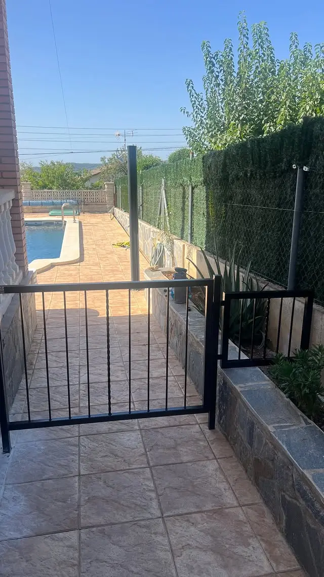 Puerta metálica negra con diseño minimalista, instalada en jardín residencial